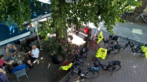 A patio area with tables and chairs, bicycles, and a tree providing shade.