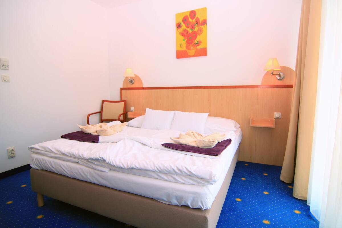 A hotel room with a bed, a nightstand, a lamp, and a painting on the wall.