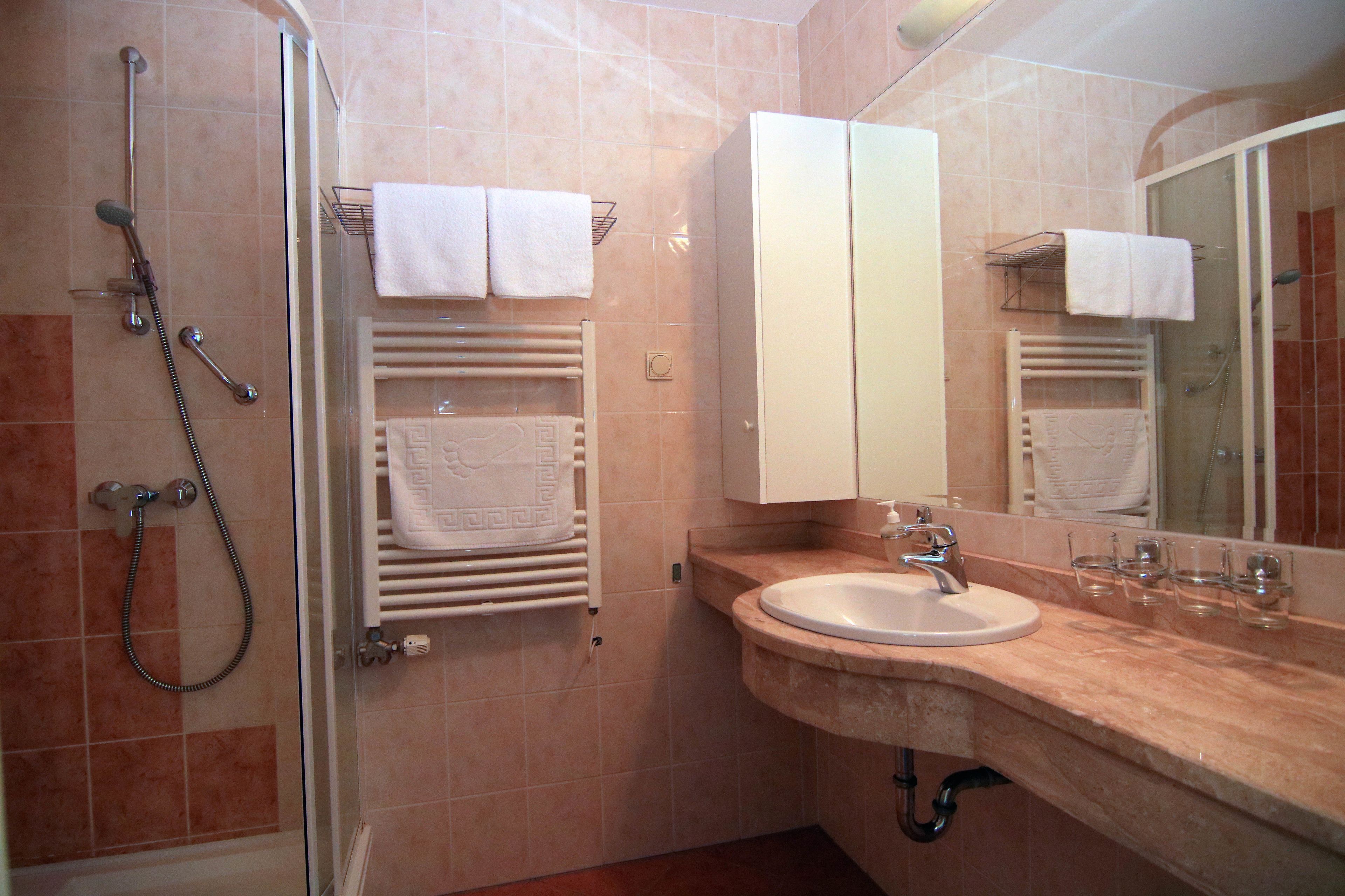 Un baño con ducha envuelta en vidrio, lavamanos con encimera de mármol y espejo con toallero.