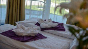 Ein Hotelzimmer mit Bett, zwei Handtüchern und Blick auf einen Garten sowie auf parkende Autos durch das Fenster.