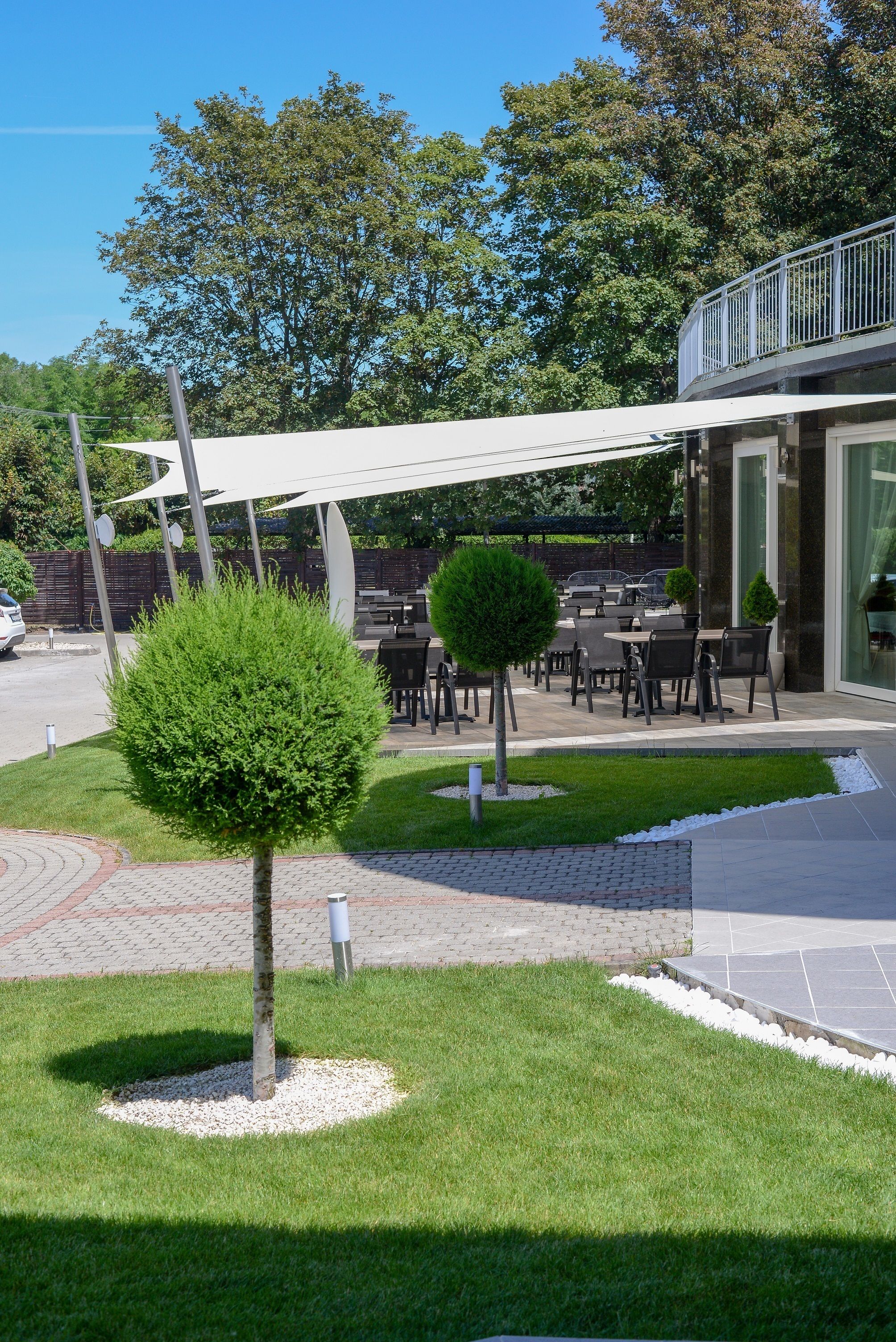 Un espace extérieur aménagé avec des tables et des chaises, entouré de pelouses et d’arbres bien entretenus.