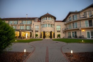 A hotel with a central entrance, multiple balconies, and a well-lit driveway. - Holiday Resorts (Balatonszarszo)