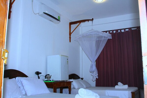 A hotel room with two beds, an air conditioning unit, a desk with a computer, and a mosquito net over one bed. - Nature Park Udawalawe (Udawalawa)
