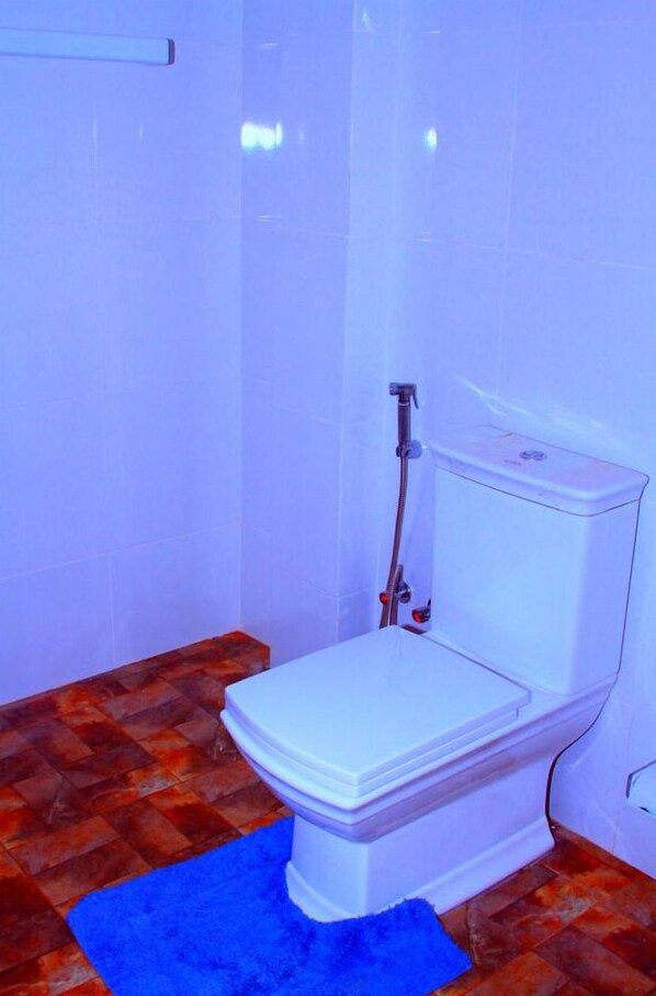 A bathroom with a white toilet, a shower, and a blue rug. - Nature Park Udawalawe (Udawalawa)