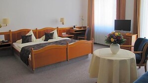 A hotel room with a wooden bed, bedside tables, a desk with a computer, a television, and a round table with a vase of flowers. - Hotel Anlage Heidelberg (Heidelberg)