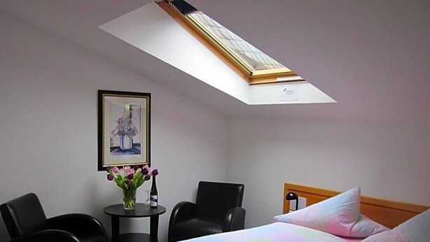 A hotel room with a bed, a desk, two chairs, a small table with a vase of flowers, and a framed picture on the wall. - Hotel Anlage Heidelberg (Heidelberg)