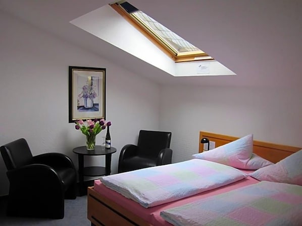 A hotel room with a bed, a desk, two chairs, a small table with a vase of flowers, and a framed picture on the wall. - Hotel Anlage Heidelberg (Heidelberg)