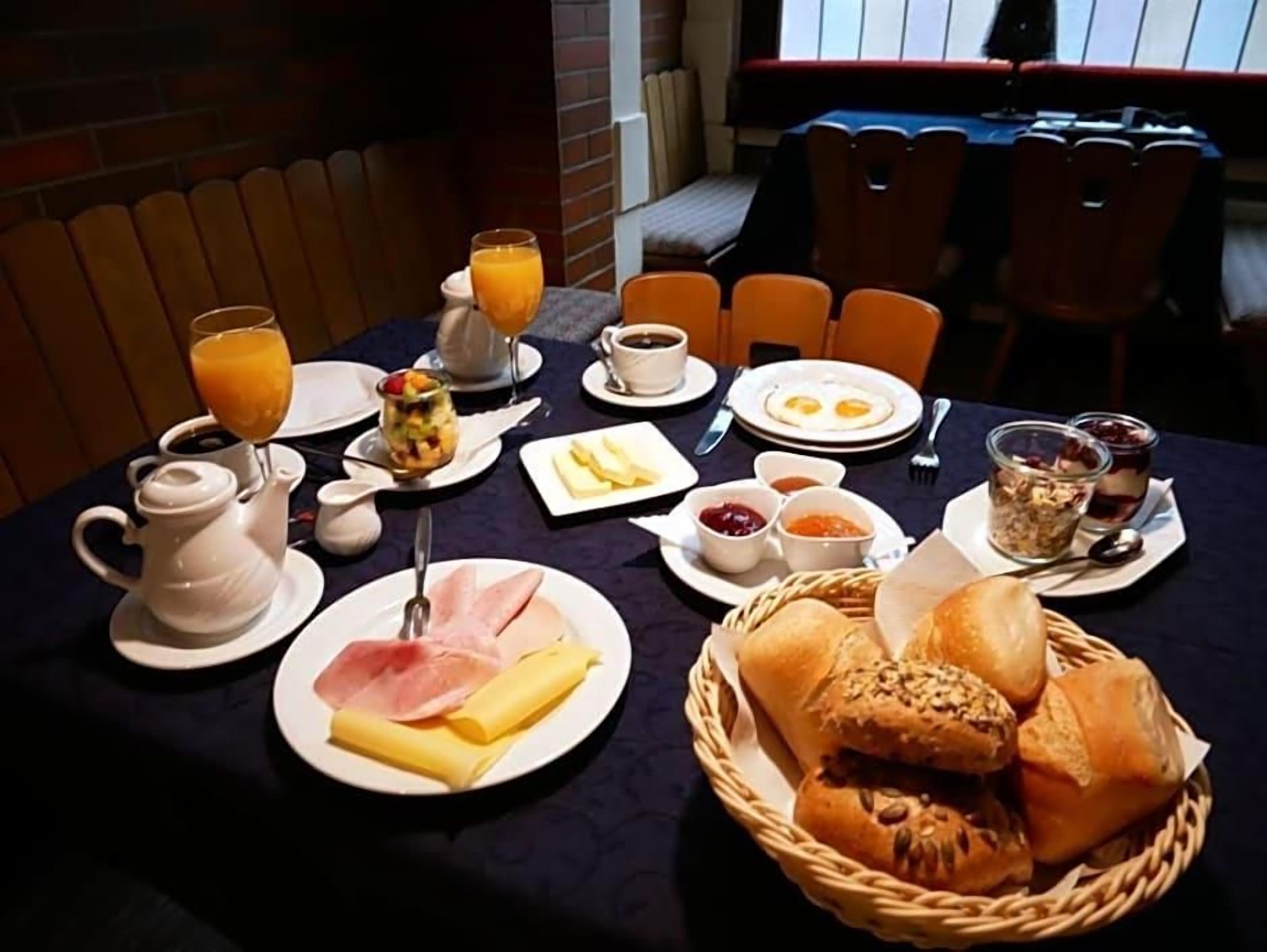 A breakfast table set with plates of food, a teapot, and a basket of bread.
