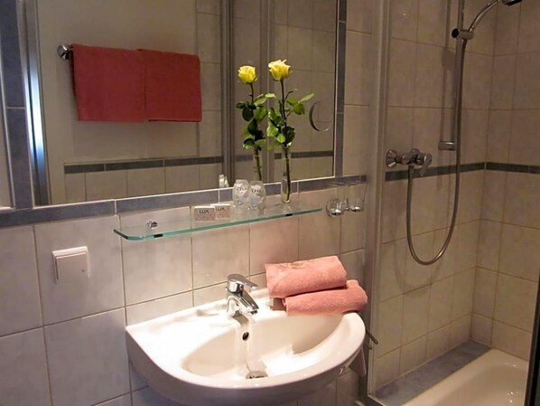 A bathroom with a white sink, a glass shelf, a mirror, a red towel, and a shower area.