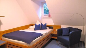 A bedroom with a bed, a chair, a nightstand, and a window. - Hotel Anlage Heidelberg (Heidelberg)