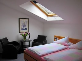 Een hotelkamer met een bed, een bureau, twee stoelen, een kleine tafel met een bloevas en een lijst aan de muur.
