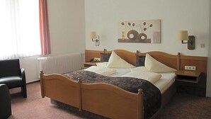 A hotel room with a wooden bed, two bedside tables, a chair, a radiator, and a window with curtains. - Hotel Anlage Heidelberg (Heidelberg)