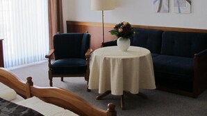 Ein Hotelzimmer mit einem Bett, einem blauen Sessel, einem runden Tisch mit Blumenvase, einer Stehlampe und zwei abstrakten Bildern an der Wand.