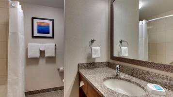 A bathroom with a granite countertop sink, a framed picture on the wall, and two white towels hanging on hooks.