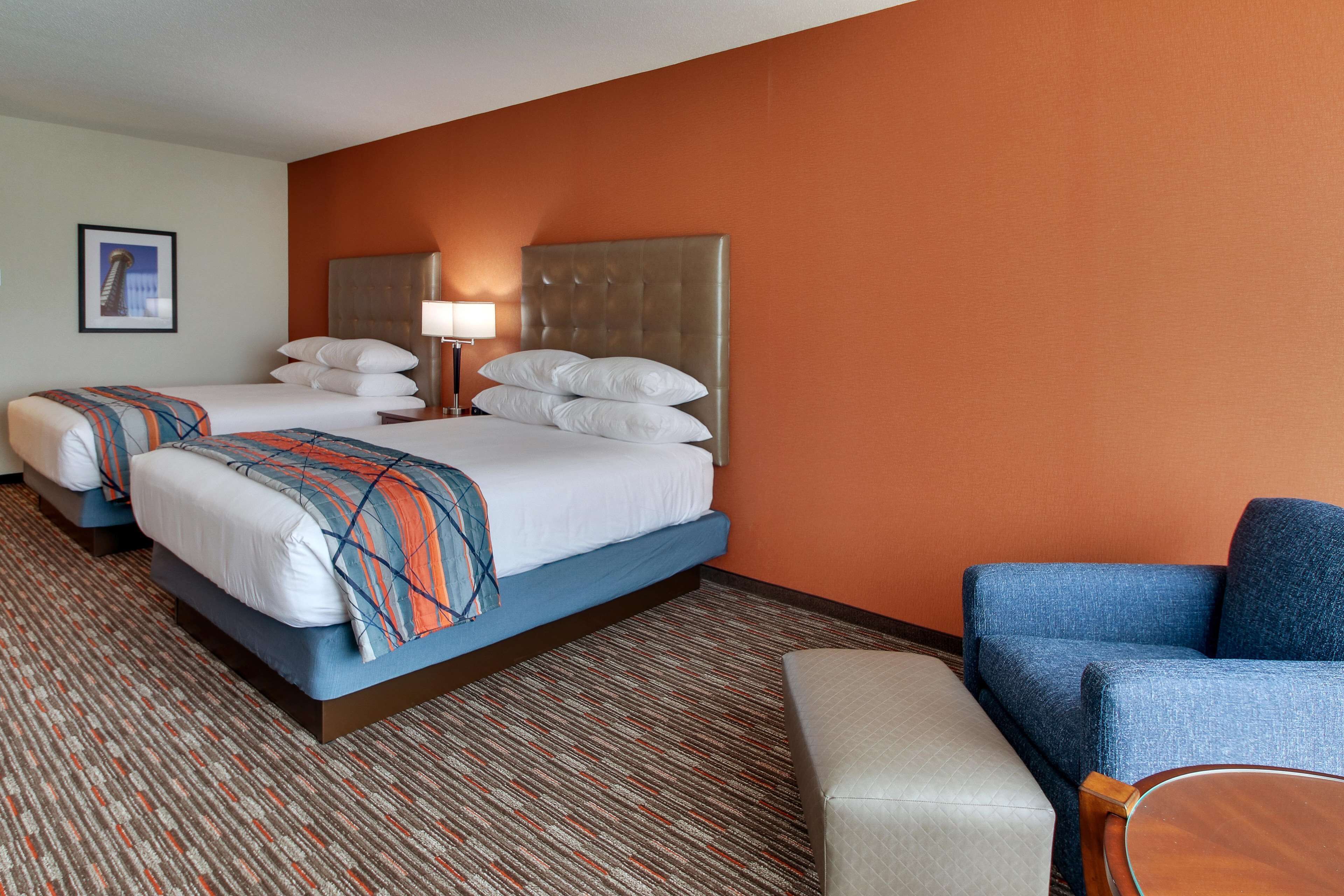 A hotel room with two beds, a blue armchair, and a small table.