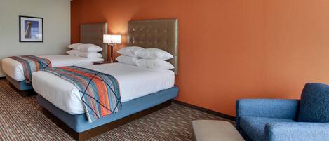 A hotel room with two beds, a blue armchair, and a small table.