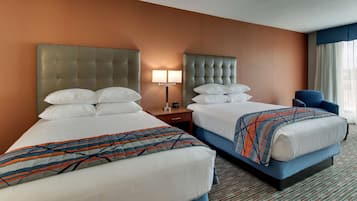 A hotel room with two beds, a nightstand, a lamp, and a chair.