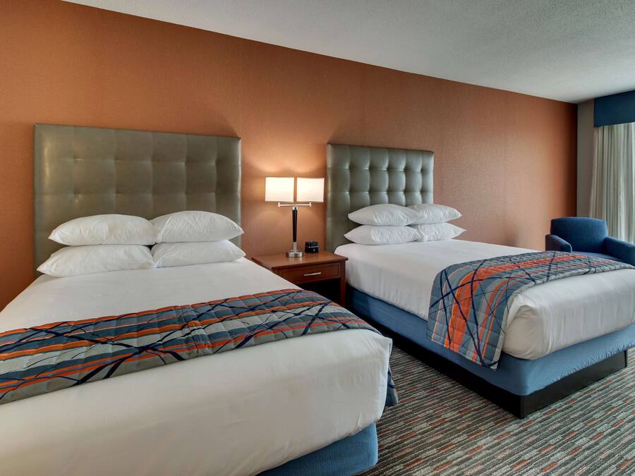 A hotel room with two beds, a nightstand, a lamp, and a chair.
