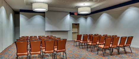 A conference room with rows of orange chairs, a projector screen, and a patterned carpet.