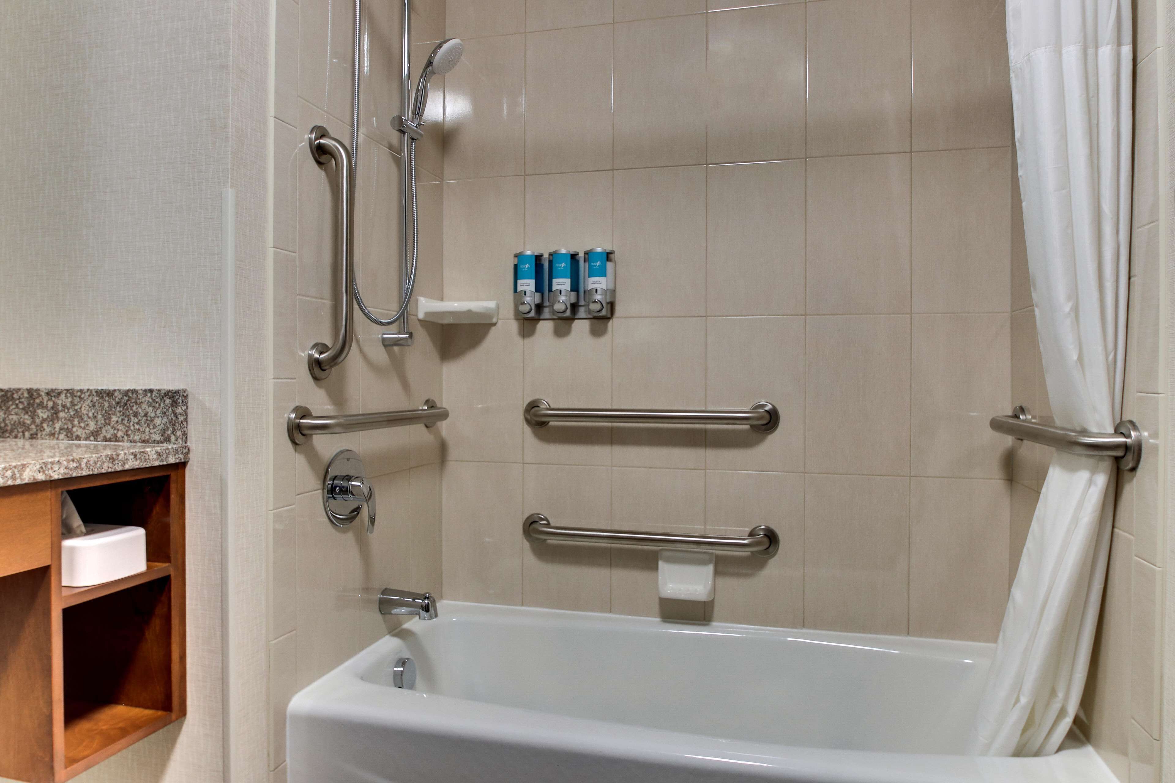 A bathroom with a bathtub, grab bars, a showerhead, and hand soap dispensers.