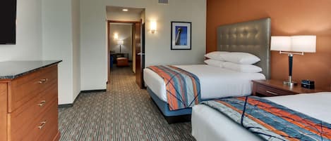 A hotel room with two beds, a wooden dresser, a desk with a lamp, and a framed picture on the wall.
