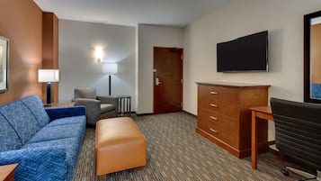 Una habitación de hotel con sofá, una mesita, escritorio, televisor y armario.