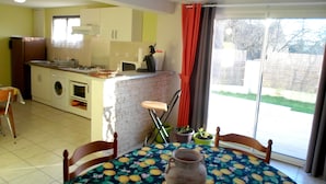 Une cuisine compacte comprenant un coin repas, un lave-linge et une table recouverte d’une nappe à motifs de fruits.