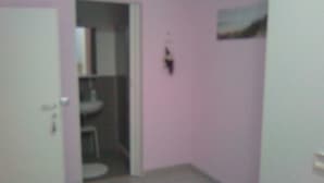 A room with a door leading to a bathroom, a small table, and a wall-mounted light fixture. - Sweet Dream (Passignano sul Trasimeno)