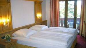 A double bed with a wooden headboard, a nightstand with a vase of flowers, and a balcony with a chair.