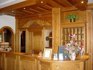A reception area with wooden paneling, a reception desk, a framed certificate, and a potted plant.