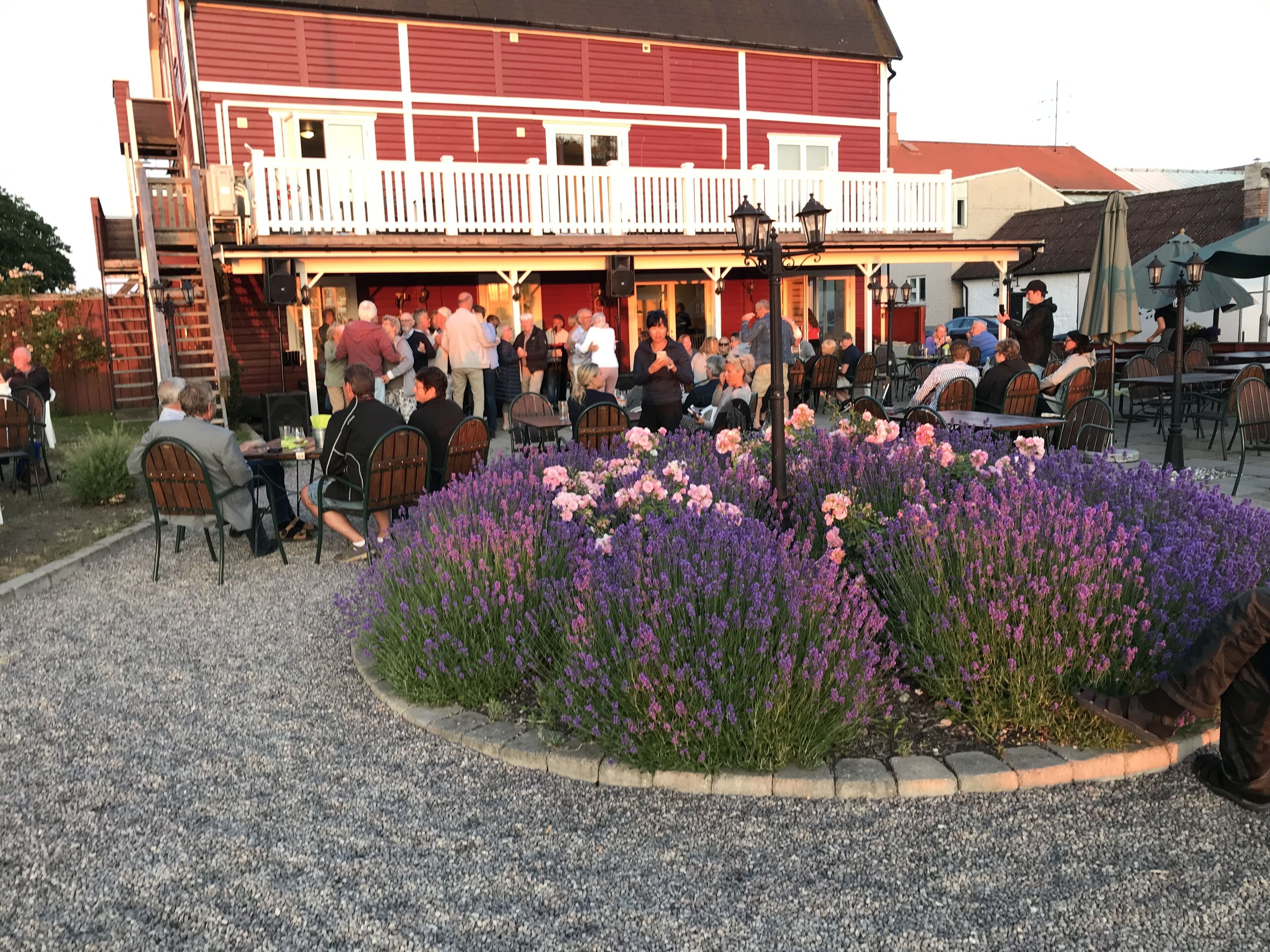 An outdoor seating area with tables and chairs, surrounded by a flower bed with purple and pink flowers.