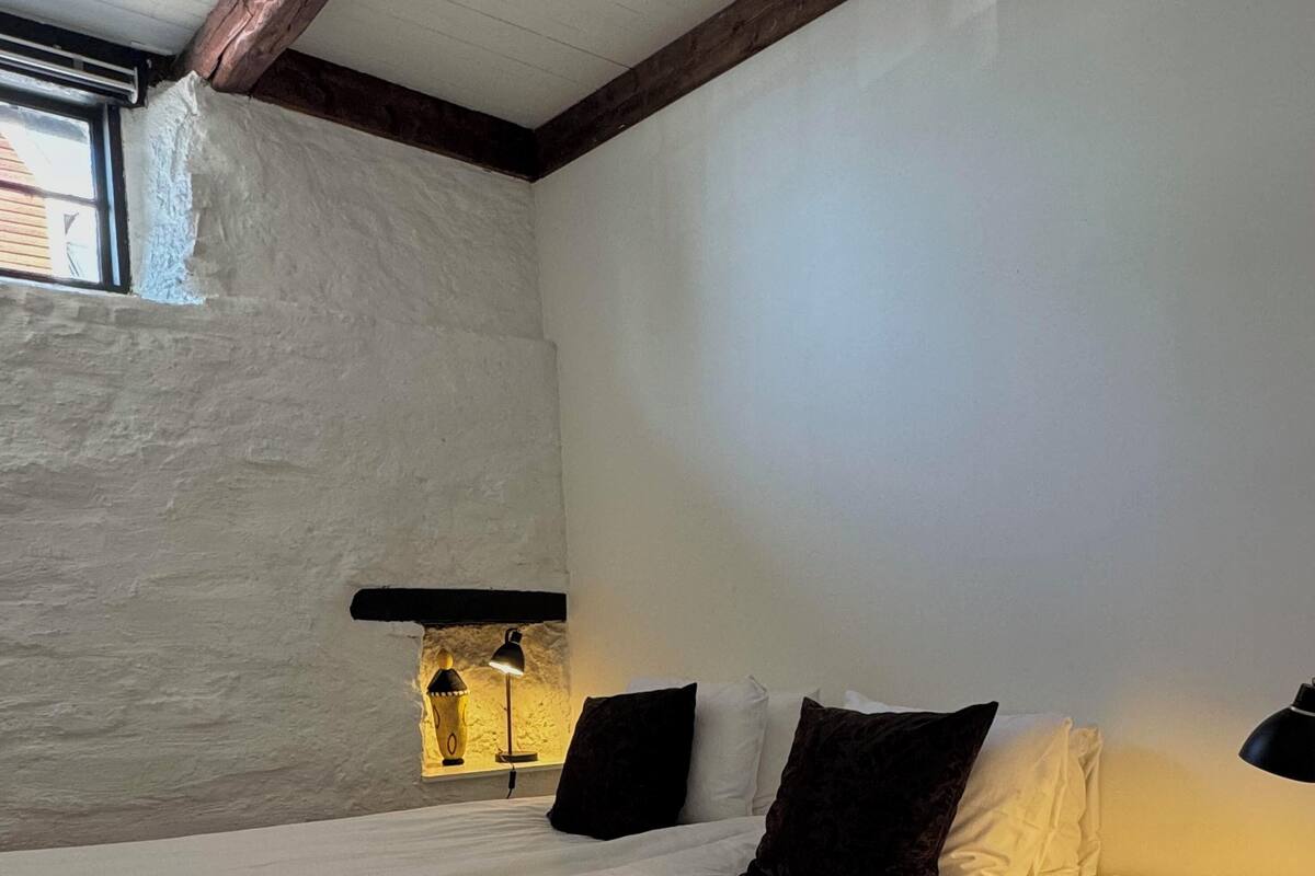 A bedroom with a large bed, a nightstand, a lamp, and a wall-mounted shelf.