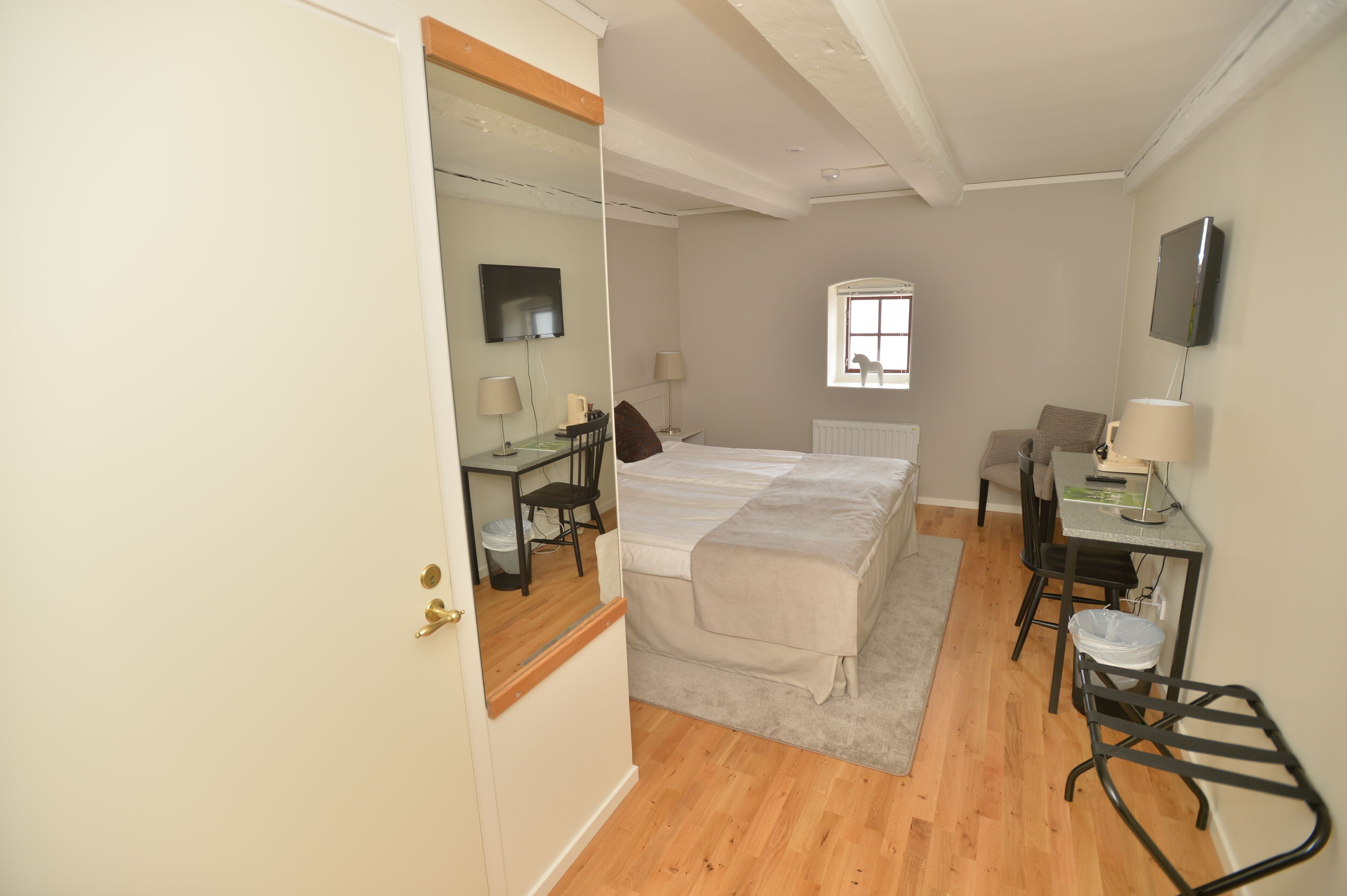 A bedroom with a bed, a desk, a chair, a TV, and a window.