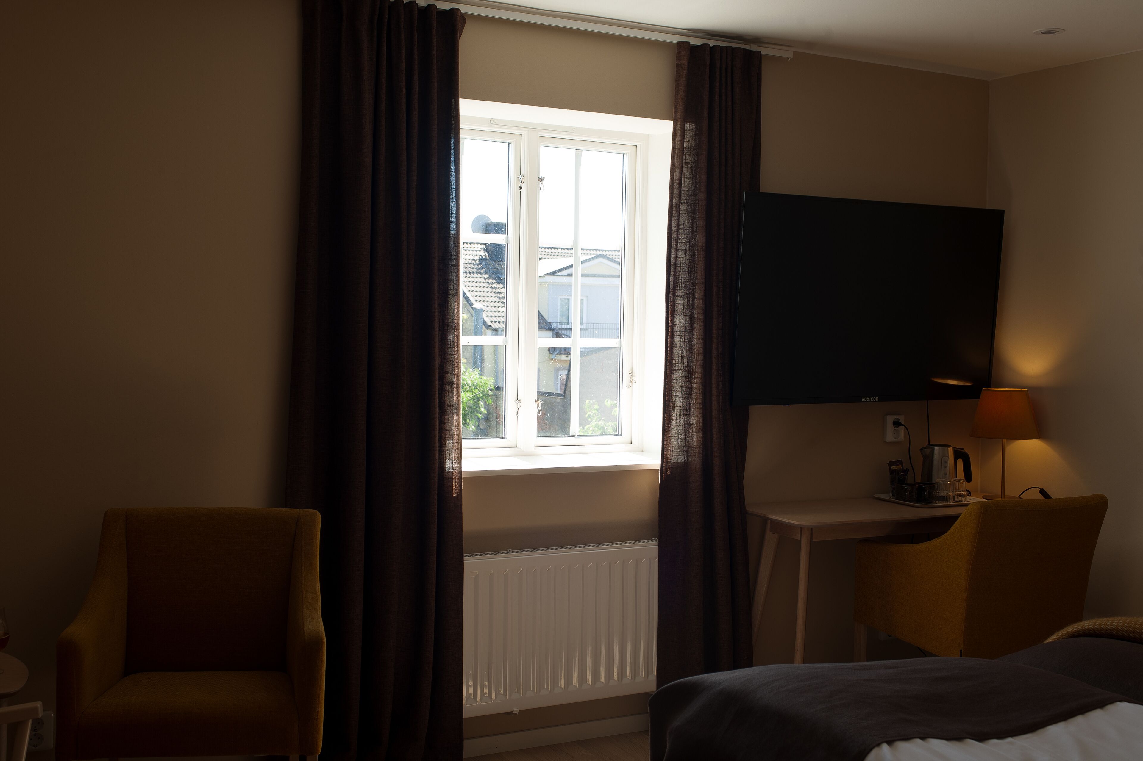 A hotel room with a bed, a desk, a chair, a TV, and a window with curtains.