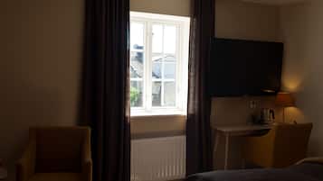 A hotel room with a bed, a desk, a chair, a TV, and a window with curtains.