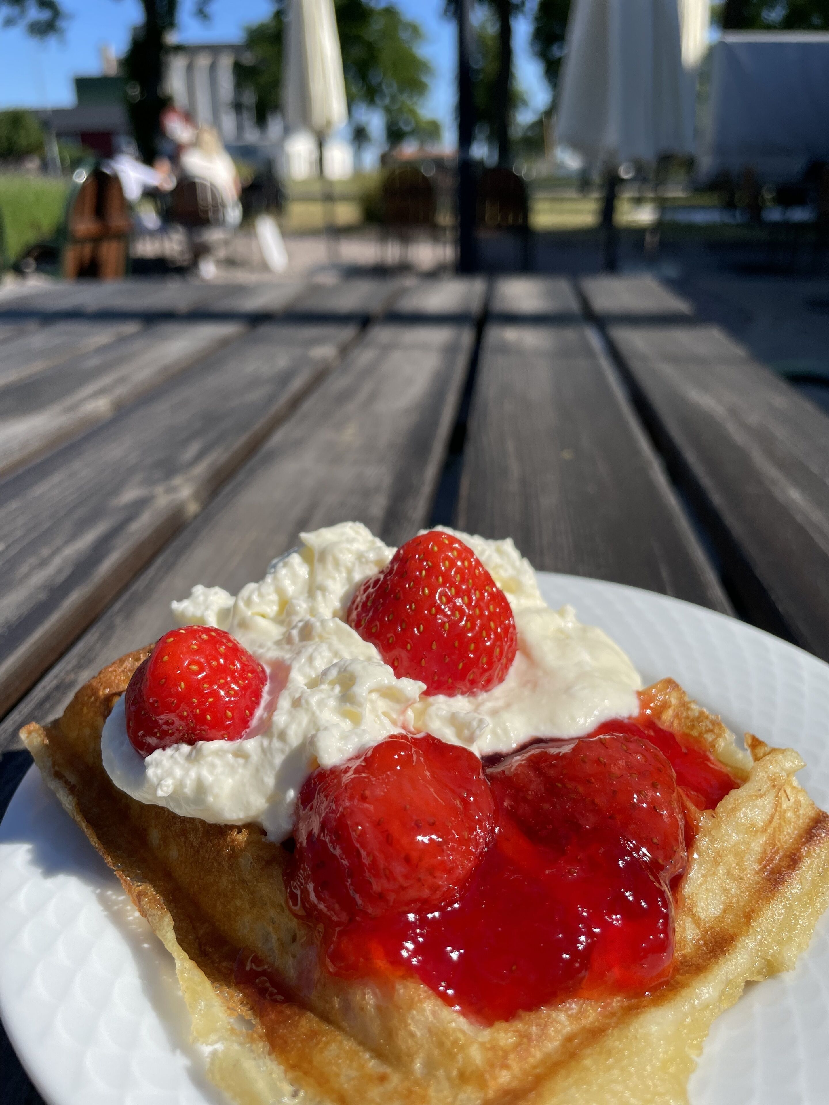 A dessert on a white plate with strawberries and whipped cream on a wooden table.