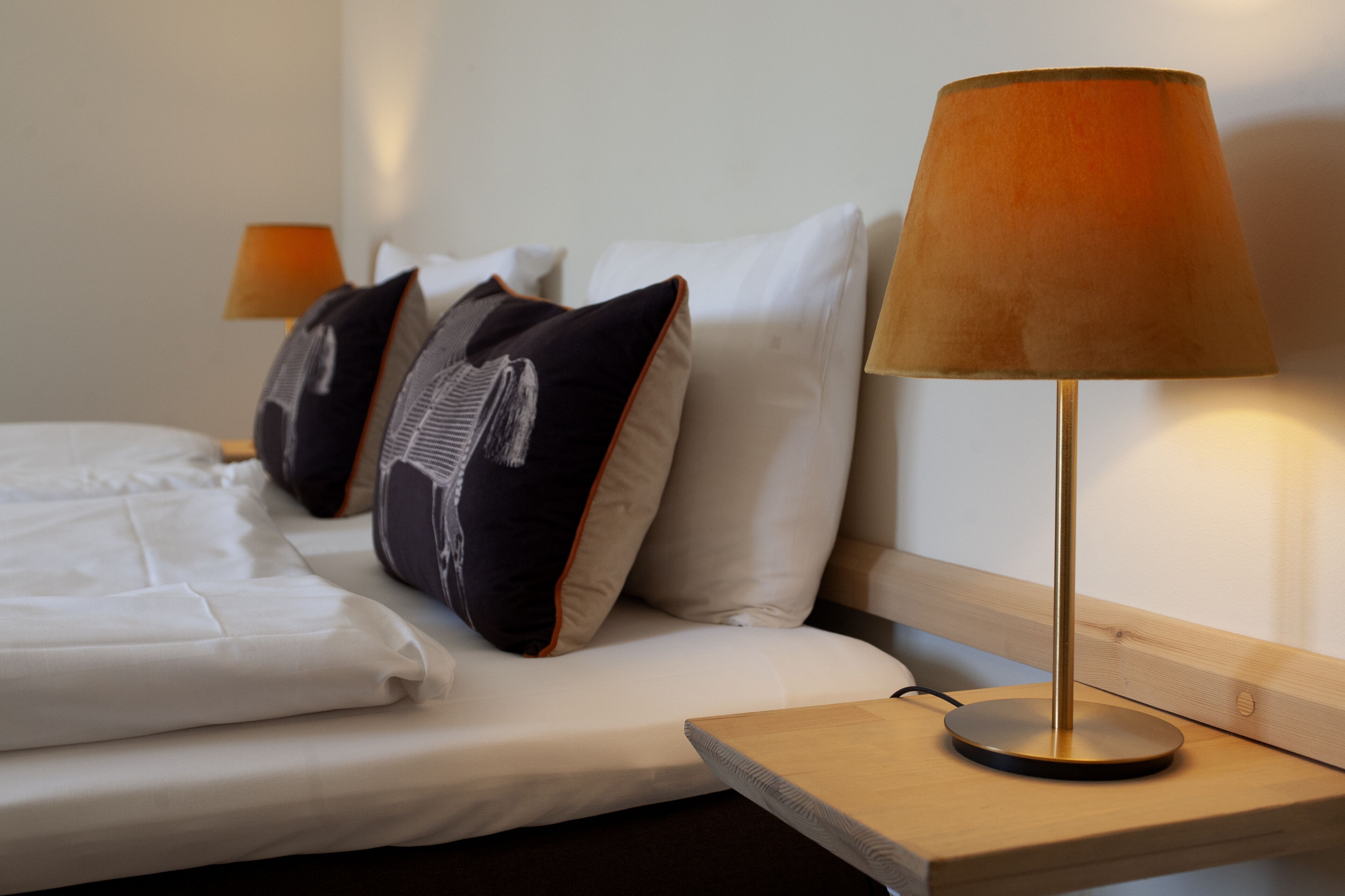 Una cama bien hecha con sábanas blancas y una mesita de noche de madera con una lámpara.