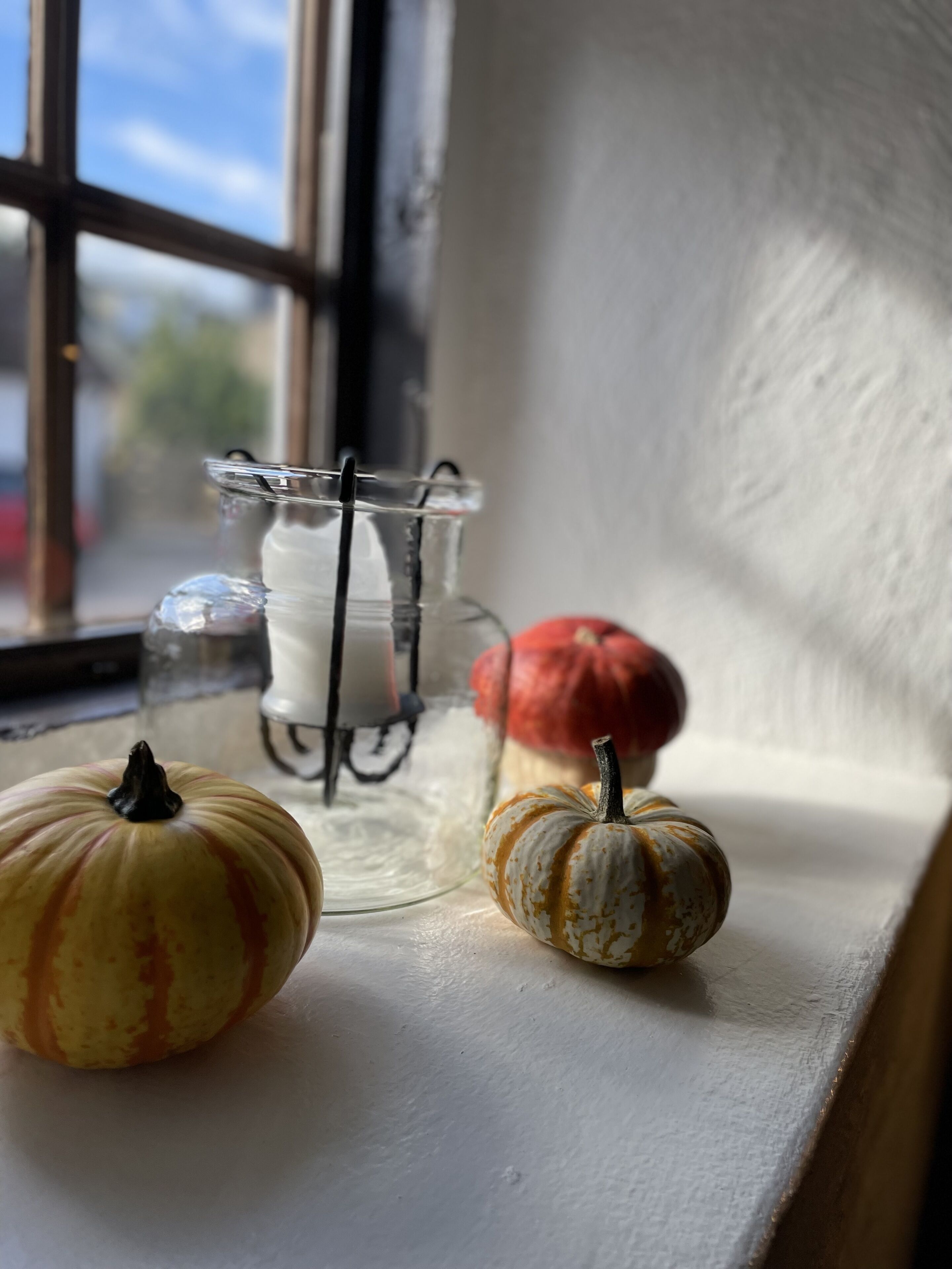 A window sill with two small pumpkins and a glass vase with a candle.