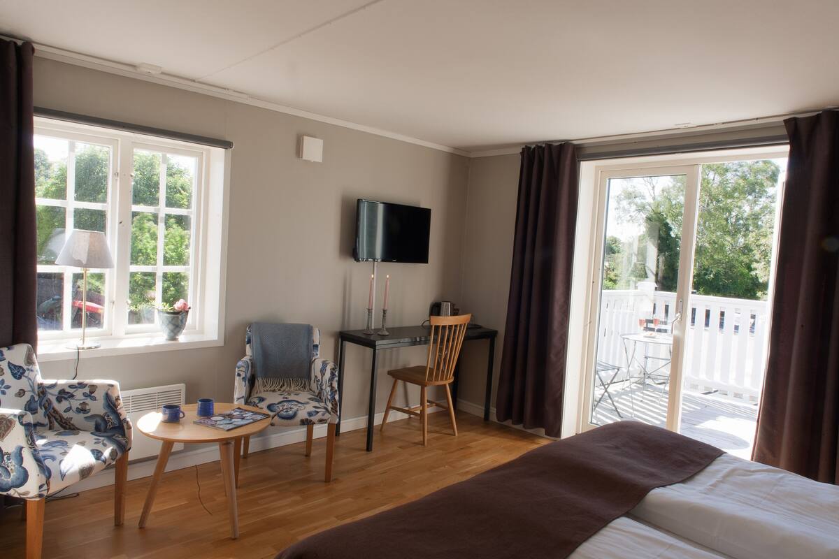 A hotel room with a bed, a desk, a chair, a table, and a TV.