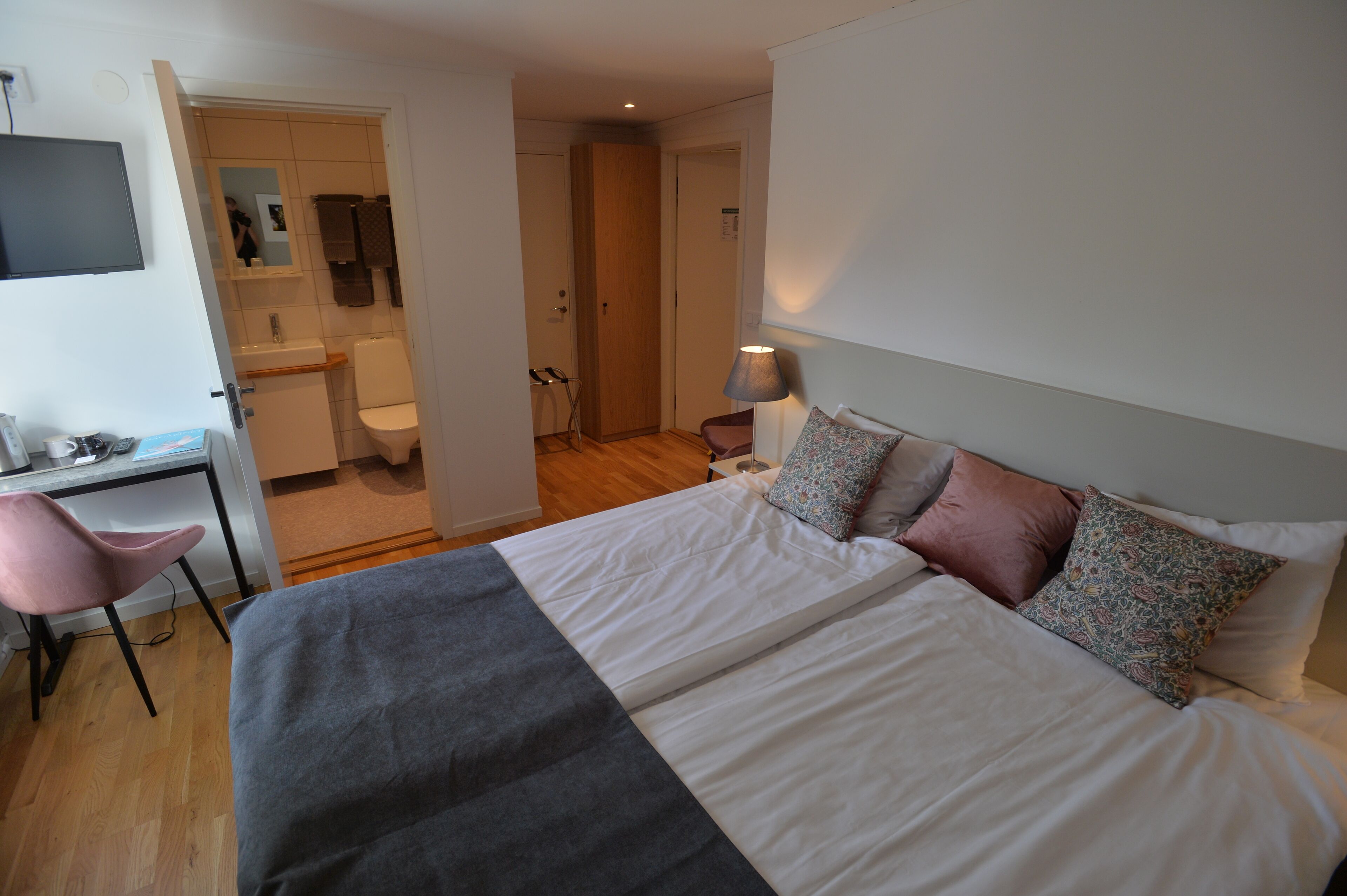 Una camera da letto con un letto, una scrivania, una sedia, una lampada e un bagno parzialmente visibile da una porta aperta.
