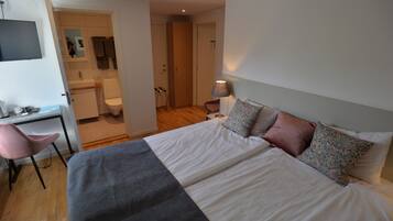 Una camera da letto con un letto, una scrivania, una sedia, una lampada e un bagno parzialmente visibile da una porta aperta.