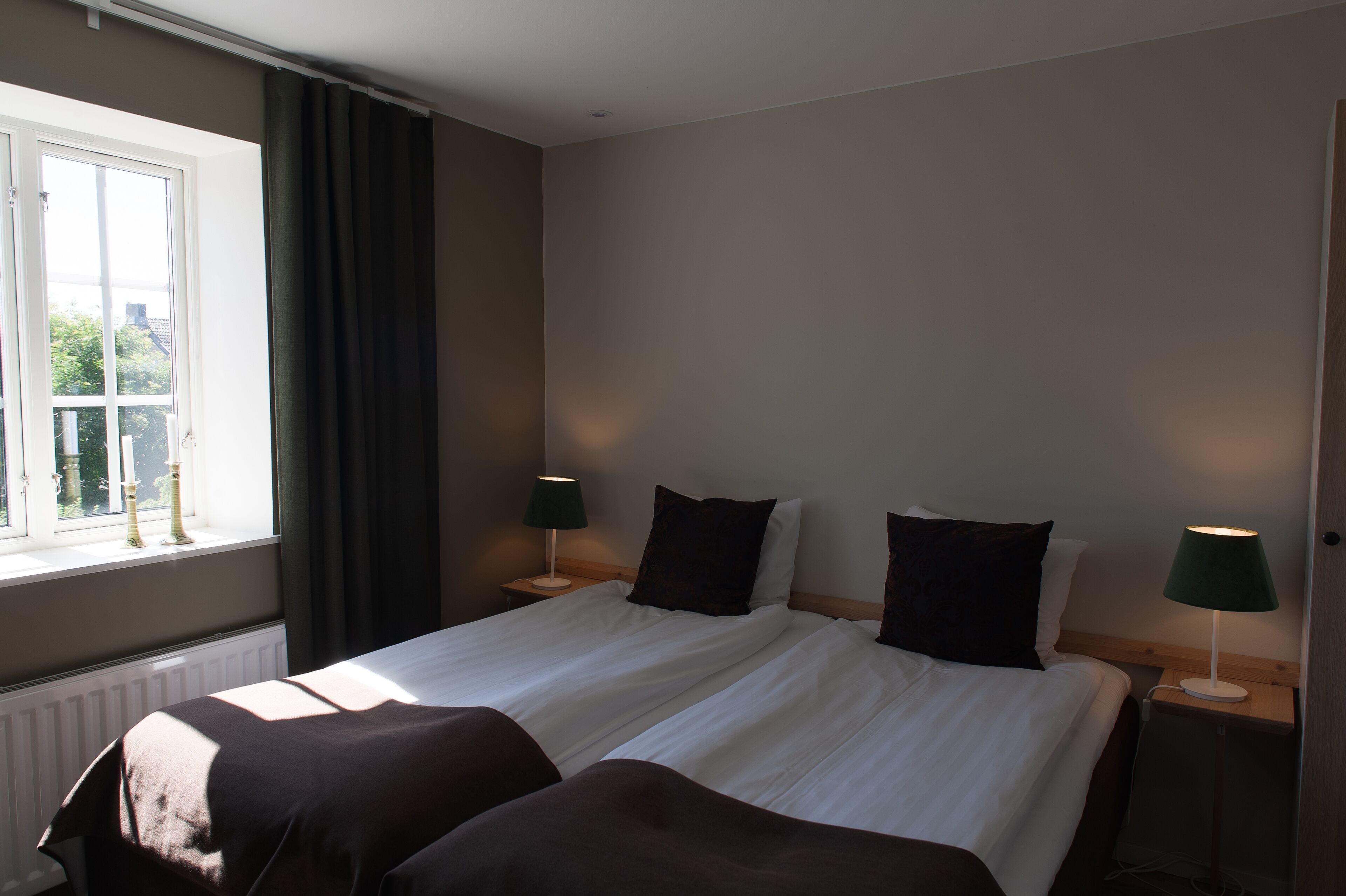 A hotel room with a large bed, two bedside tables, a window with curtains, and a radiator.