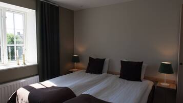 A hotel room with a large bed, two bedside tables, a window with curtains, and a radiator.