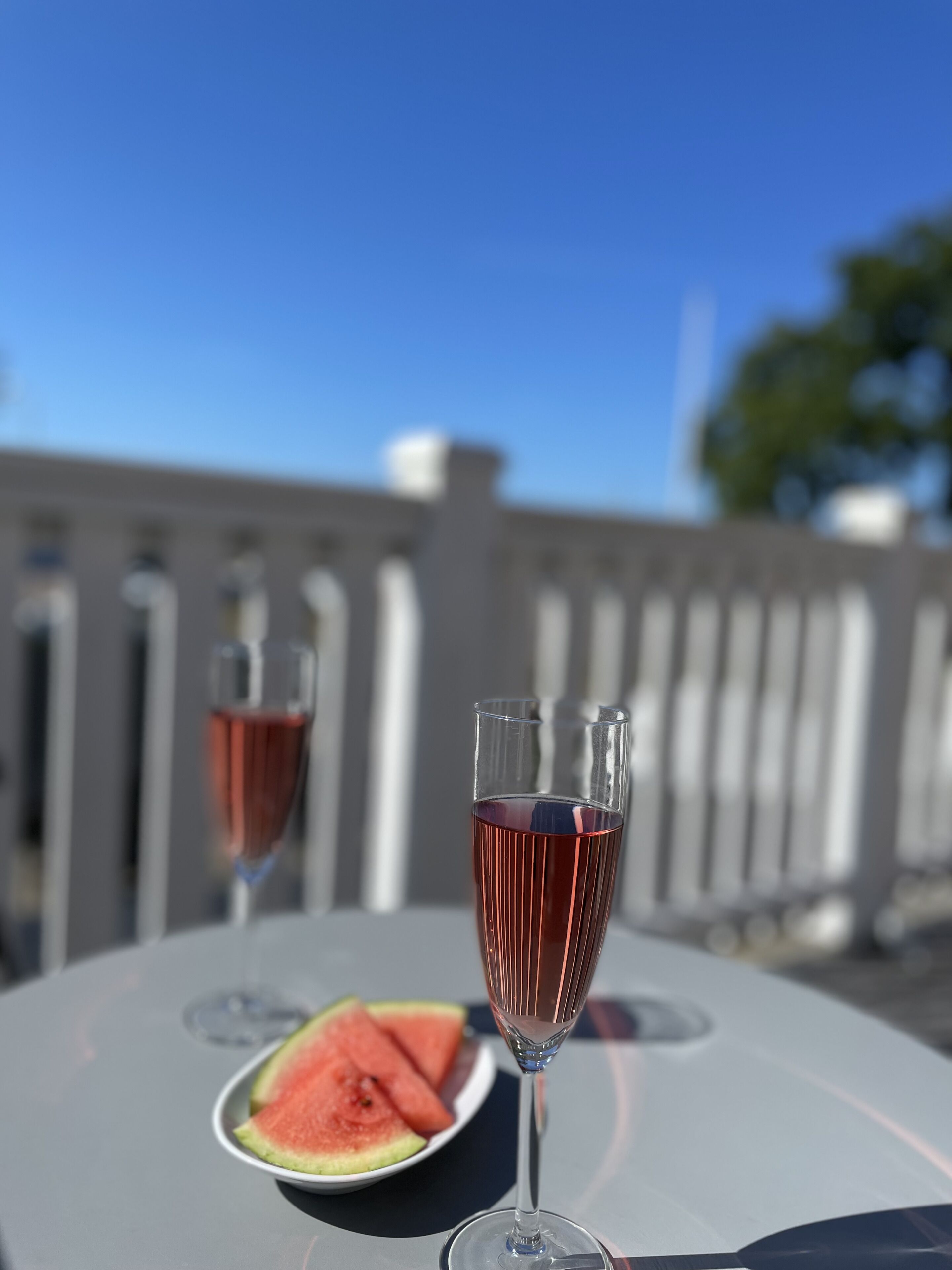 A table with two glasses of red wine and a plate of watermelon slices.