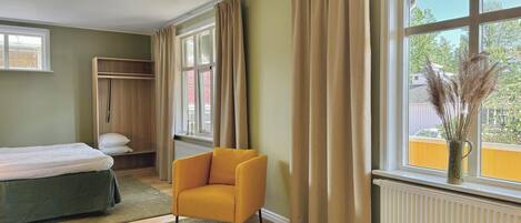 A bedroom with a bed, a yellow armchair, a wardrobe, and a window with curtains.