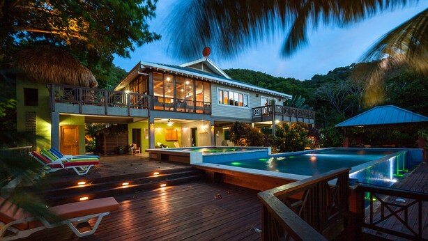 A two-story house with a swimming pool, wooden deck, and lounge chairs. - Springwater Resorts (Roatan)