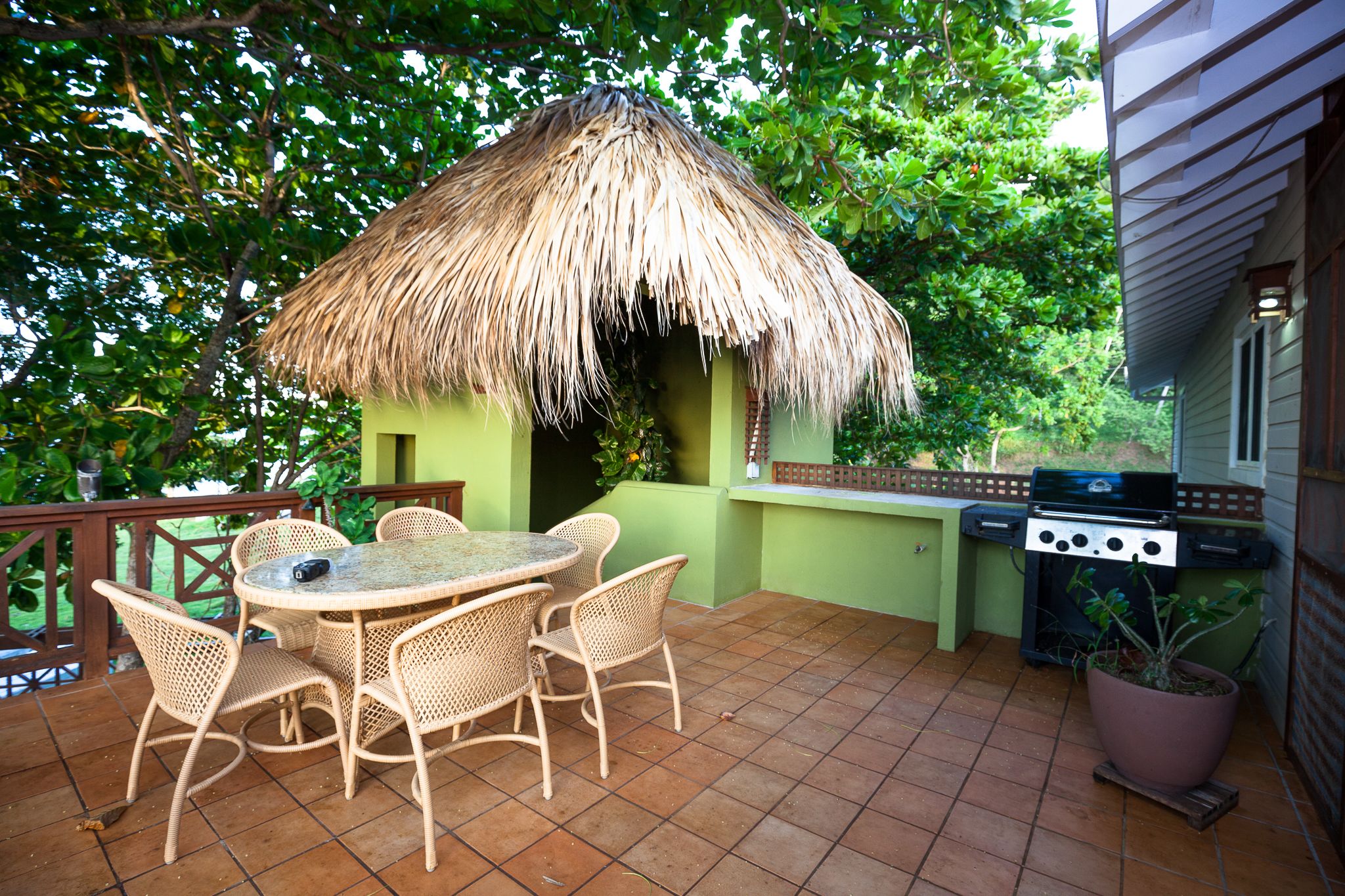 An outdoor patio with a thatched-roof structure, wicker furniture, and a grill.