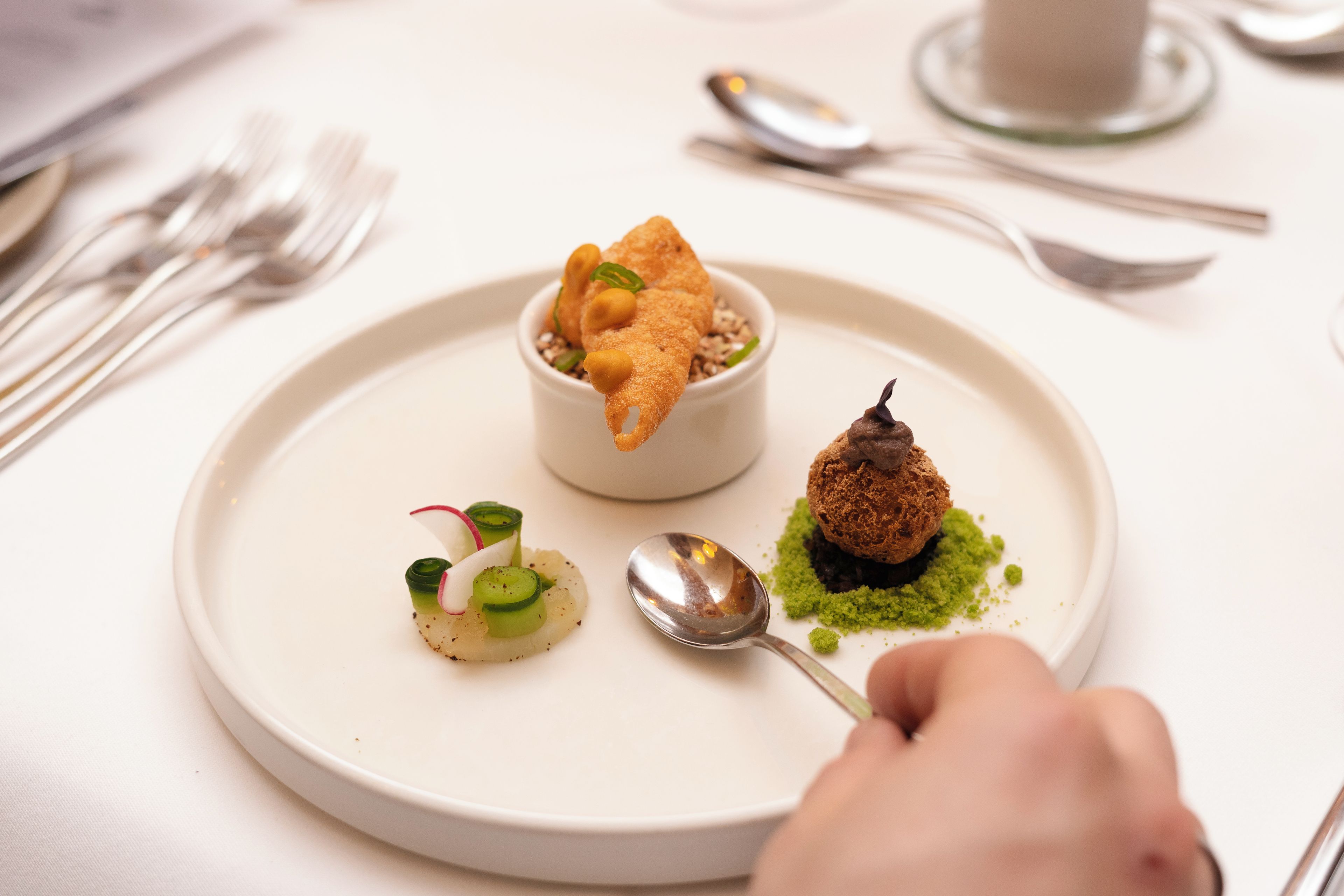 A white plate with a variety of food items, including a small bowl, a spoon, and a piece of food on a green base.