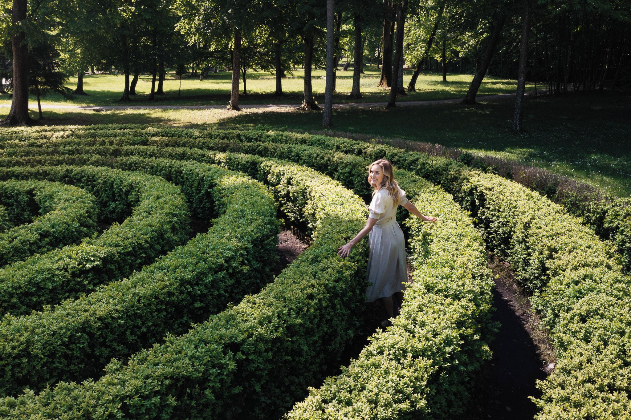 A person standing in a garden with a maze of trimmed hedges.