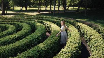 A person standing in a garden with a maze of trimmed hedges.